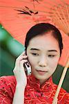 Young woman wearing traditional Chinese clothing, holding parasol and using cell phone