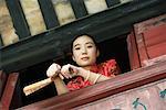 Jeune femme portant des vêtements traditionnels chinois, tenir ventilateur, s'appuyant sur le rebord d'une fenêtre, vue d'angle faible