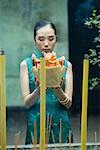 Young woman standing in temple courtyard, holding up religious offering, eyes closed