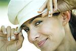 Woman adjusting hat, smirking at camera, close-up