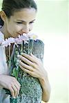 Woman leaning on wooden post, smelling flowers