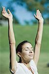 Woman outdoors in sun with arms raised, smiling, eyes closed