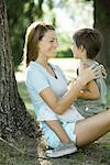 Mother and son outdoors, boy sitting on woman's lap