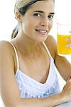 Woman holding up glass of orange juice, smiling at camera