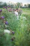 Young woman standing in flower garden, waving, in mid distance