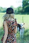 Young woman in sundress walking toward cow, rear view