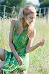 Jeune femme en robe accroupi dans champ, regardant le brin d'herbe