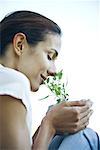 Woman holding herb in cupped hands, smelling it with eyes closed, close-up