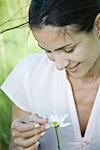 Woman holding flower, looking down, smiling, close-up