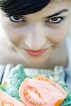 Young woman leaning face over cut up tomatoes, smiling at camera, close-up