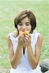 Young woman smelling piece of fruit, eyes closed