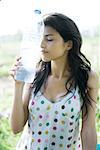 Young woman holding bottle of water against forehead, eyes closed