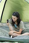 Teen girl sitting in tent, holding cell phone