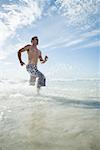 Young man running through surf, low angle view
