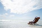 L'homme assis dans une chaise longue sur la plage, surfer à laver sous lui, vue arrière