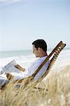 Homme assis dans une chaise longue sur la plage, lecture de journal