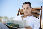 Jeune homme lisant journal en chaise longue