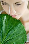 Young woman holding leaf up to face, close-up, cropped