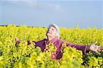 Senior woman standing in field, arms out and head back