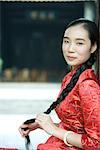 Young woman dressed in traditional Chinese clothing, holding her long braided hair, looking at camera