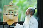 Elderly man in traditional Chinese clothing, looking at birds in bird cage