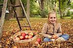 Portrait de jeune fille assise à l'automne les feuilles avec panier de pommes