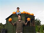 Boy Sitting on Top of Shed with Feet on Father's Head