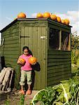 Girl Holding Pumpkins in Front of Shed