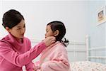 Mother helping her daughter to wear a bathrobe in the bedroom