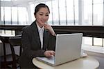 Young woman sitting by laptop, smiling