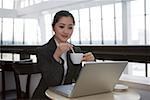 Young woman sitting by laptop and holding coffee cup