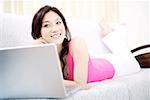 Young woman lying by a laptop, smiling