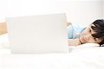 Portrait of a young woman relaxing on bed by laptop