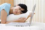 Young woman lying on bed and looking at laptop