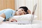 Young woman lying on bed and looking at laptop