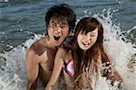 Young couple playing in wave, smiling