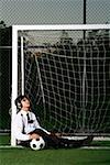 Young man with headphones sitting by goal post
