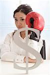 Portrait of a young woman wearing boxing glove with dollar sign in foreground