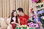 Young couple sitting together by Christmas tree, smiling