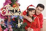 Portrait of young couple sitting with rose by Christmas tree