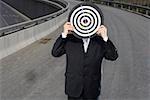 Man holding dartboard in front of face on an overpass