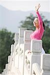 Young woman smiling with hand raised by fence