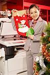 Office woman holding Christmas sock beside copy machine and Christmas tree