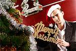 Portrait of a young man by Christmas tree holding merry Christmas in script