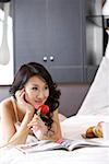 Young woman lying on bed and smelling rose, smiling