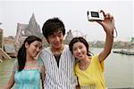Young friends taking self portrait with digital camera at amusement park, smiling