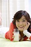 Young woman holding milk glass in bed, smiling
