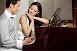 Young couple playing grand piano, smiling