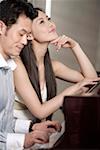 Young couple playing grand piano, smiling