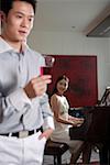 Woman playing piano with man holding wineglass in the foreground